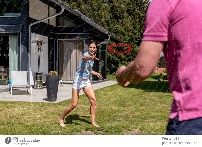 Happy couple playing with flying disc in garden of their home frisbee Playing Discs house houses twosomes partnership couples gardens domestic garden building