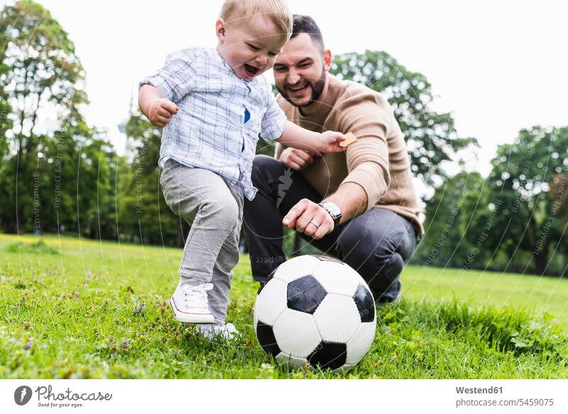 Happy father playing football with son in a park sons manchild manchildren active happiness happy parks soccer fathers daddy dads papa family families people