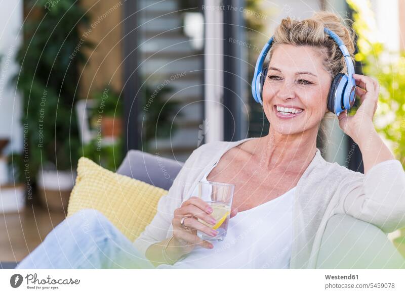 Portrait of happy mature woman sitting on terrace listening music with headphones Crockery Tableware Drinking Glass Drinking Glasses cushions couches settee
