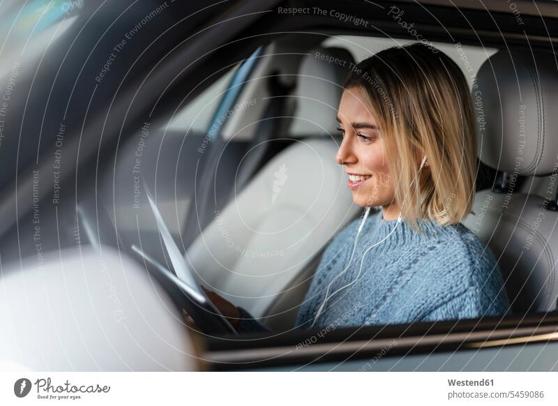 Smiling young woman with documents, tablet and earphones in a car paper papers transport motor vehicles road vehicle road vehicles Auto automobile Automobiles