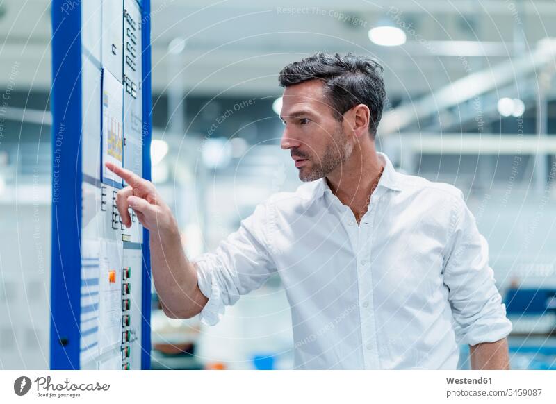 Male professional checking plans on bulletin board in industry color image colour image indoors indoor shot indoor shots interior interior view Interiors