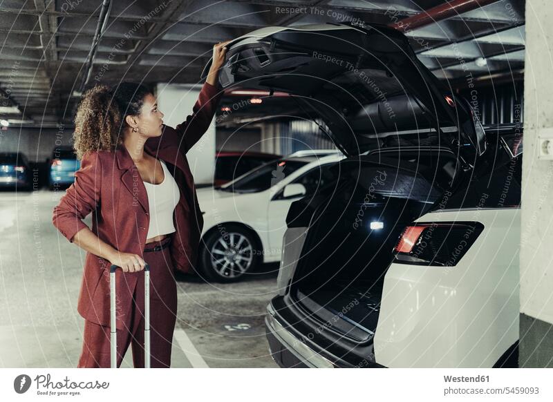 Young female professional on business trip closing car trunk at parking garage color image colour image Spain indoors indoor shot indoor shots interior