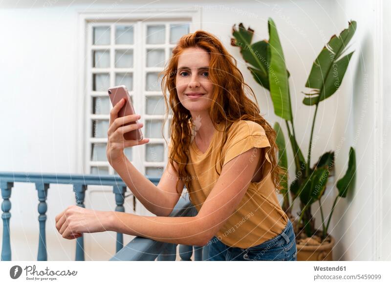 Portrait of smiling redheaded young woman with smartphone leaning on railing T- Shirt t-shirts tee-shirt telecommunication phones telephone telephones