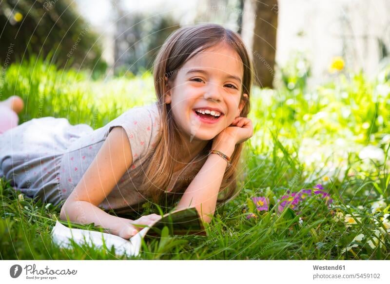 Smiling girl lying on meadow, reading a book meadows laughing Laughter laying down lie lying down books leisure free time leisure time smiling smile positive