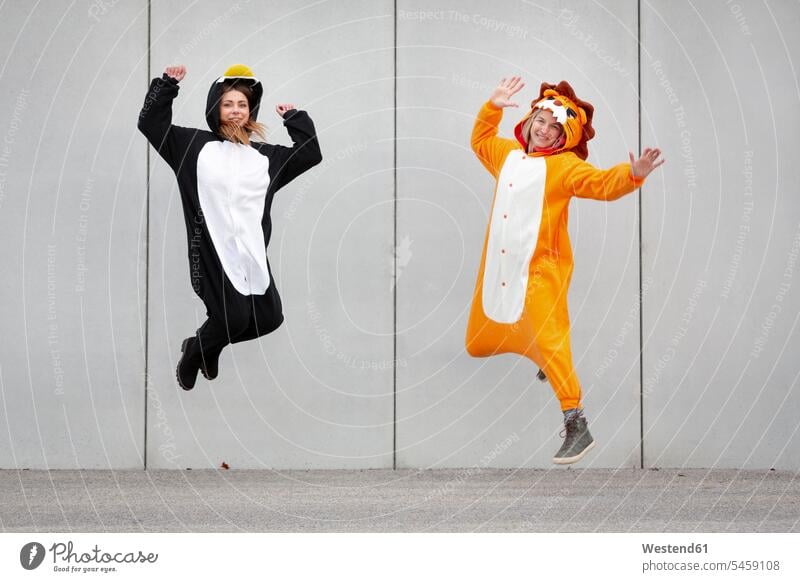 Two women in penguin and lion costume jumping in front of concrete wall leo lions celebrate partying smile Ardor Ardour enthusiasm enthusiastic excited delight