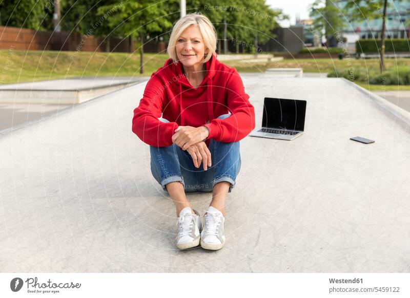 Senior woman wearing red hoodie sitting outdoors with laptop females women Seated Laptop Computers laptops notebook smiling smile confidence confident Hoodie