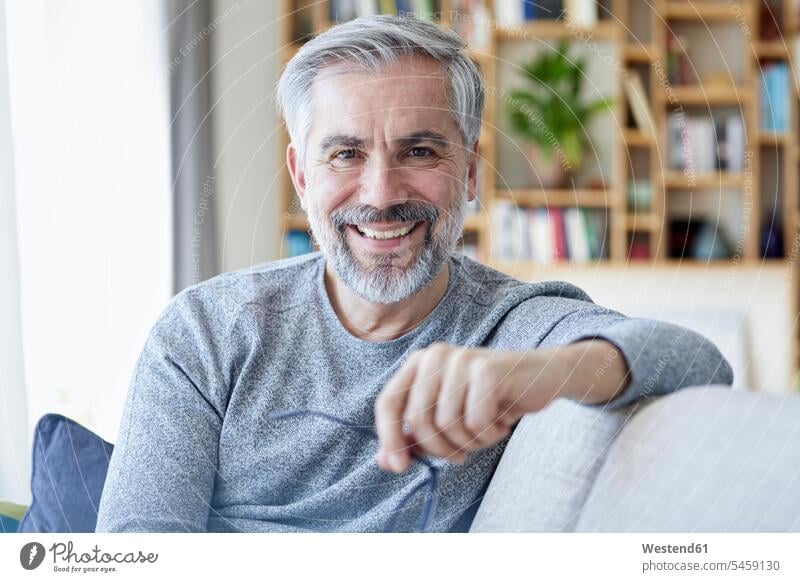 Portrait of smiling mature man sitting on couch at home men males settee sofa sofas couches settees portrait portraits smile Seated Adults grown-ups grownups