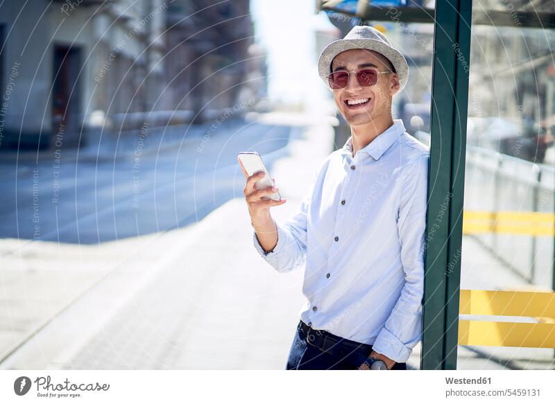 Happy young man with cell phone at a tram stop in the city Mixed Race Person mixed-race Person mixed race ethnicity wireless Wireless Connection