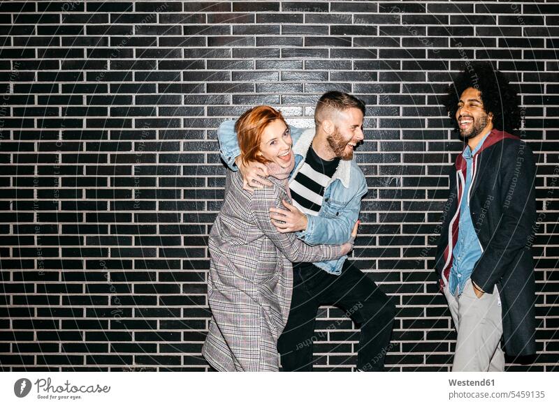 Three happy playful friends at a black wall happiness walls standing friendship colour colours brick wall brick walls fashionable Spain togetherness carefree