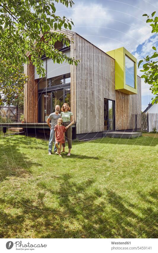 Family standing on grassy land in front of tiny house color image colour image Germany leisure activity leisure activities free time leisure time