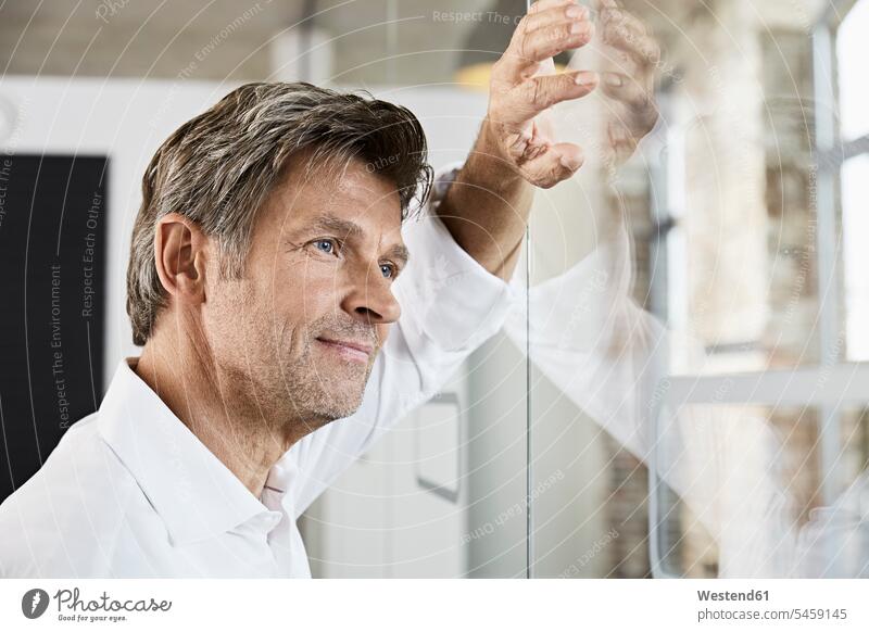 Portrait of mature businessman leaning against glass wall in office looking view seeing viewing offices office room office rooms glass pane glass panes