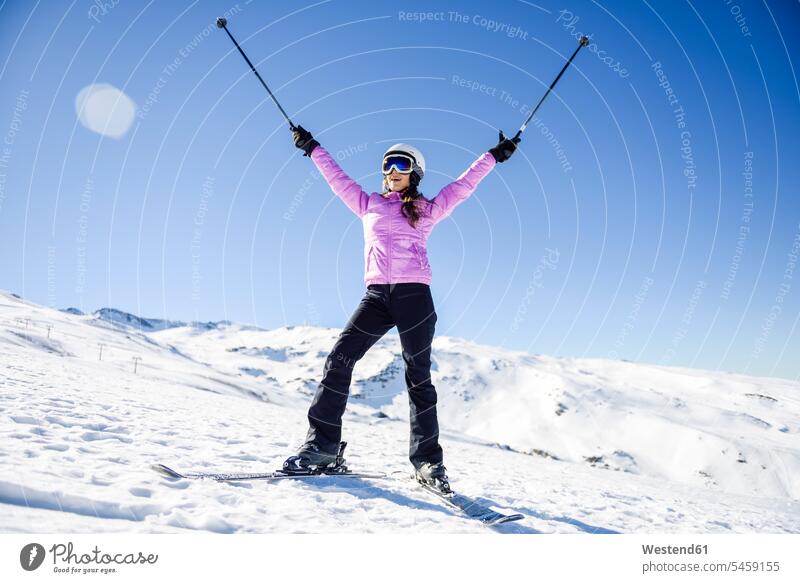 Happy woman raising her ski poles in snow-covered landscape in Sierra Nevada, Andalusia, Spain Province of Granada Ski Area ski-region skiing region clear sky