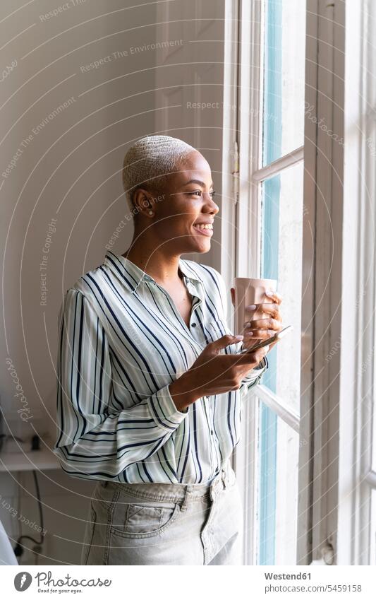Happy woman with cell phone and coffee cup looking out of window business life business world business person businesspeople business woman business women