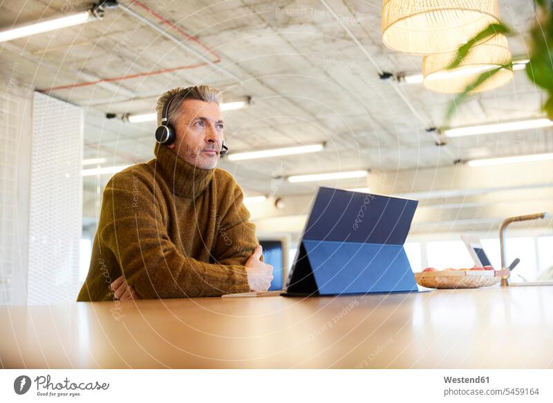 Thoughtful businessman with headset and digital tablet looking away while sitting at office color image colour image indoors indoor shot indoor shots interior