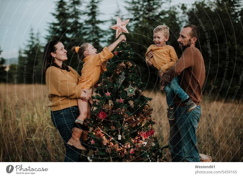 Parents carrying happy children decorating Christmas tree at countryside during sunset color image colour image Spain outdoors location shots outdoor shot