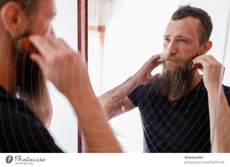 Mid adult man brushing beard with comb while looking at mirror in living room color image colour image indoors indoor shot indoor shots interior interior view