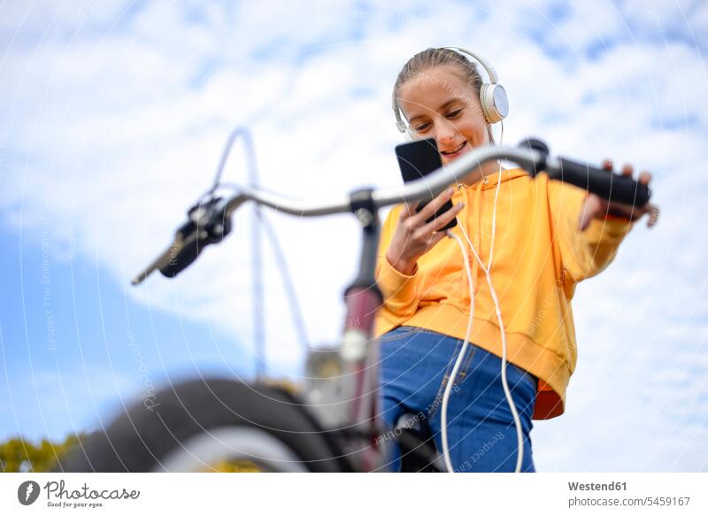 Smiling girl with headphones and bicycle looking at smartphone bikes bicycles females girls Smartphone iPhone Smartphones view seeing viewing smiling smile