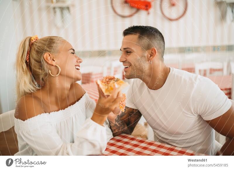 Happy young couple eating pizza while sitting in restaurant color image colour image Spain leisure activity leisure activities free time leisure time
