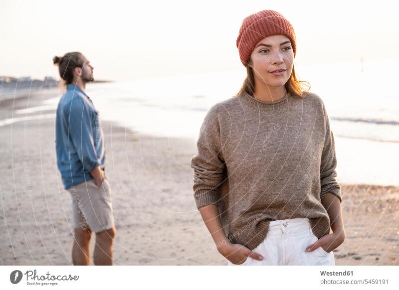 Beautiful young woman standing with hands in pockets against boyfriend at beach during sunset color image colour image Netherlands Holland The Netherlands