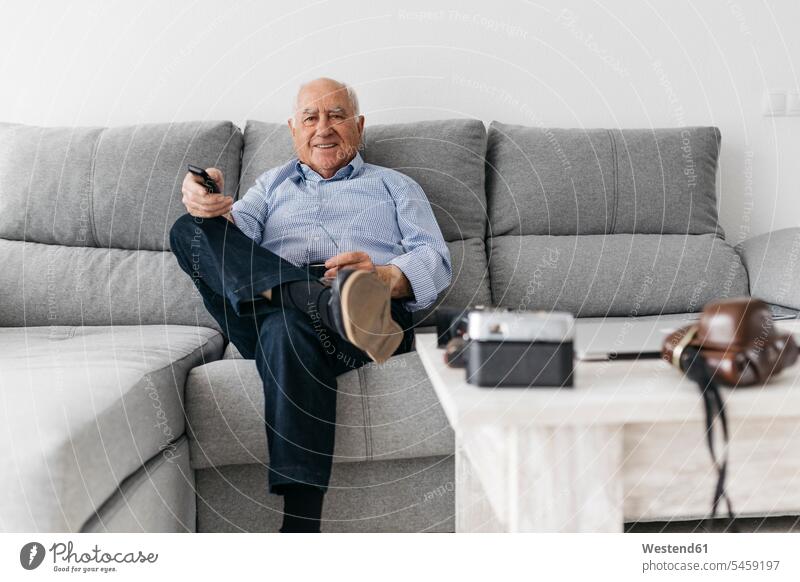 Senior man watching TV from the couch at home settee sofa sofas couches settees senior men senior man elder man elder men senior citizen hobby hobbies