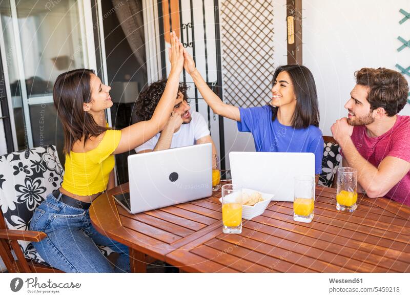 Young women giving high-five while sitting with male friends at back yard color image colour image Spain friendship bonding community day daylight shot