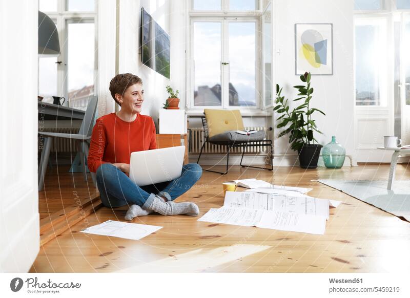 Woman sitting cross-legged on floor of her home, using laptop using a laptop Using Laptops working At Work Seated document paper documents papers tailor seat