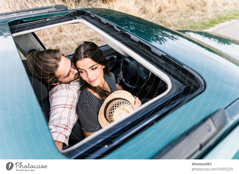 Affectionate young couple in a car seen through sunroof automobile Auto cars motorcars Automobiles twosomes partnership couples motor vehicle road vehicle