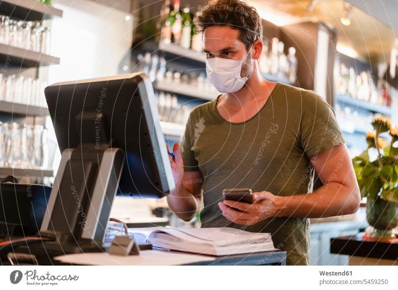 Restaurant manager with protective mask using computer and smartphone human human being human beings humans person persons caucasian appearance