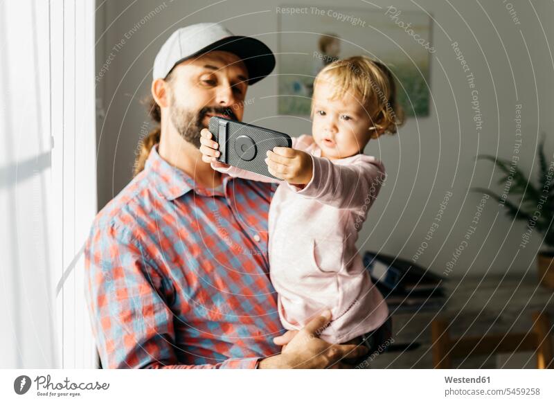 Father holding his little daughter on his arm, playing with his smartphone Smartphone iPhone Smartphones daughters father pa fathers daddy dads papa carrying