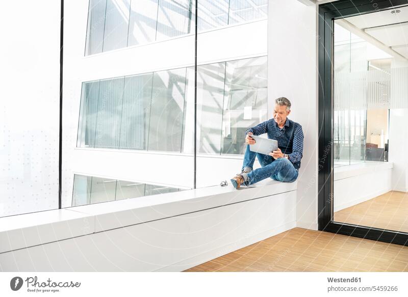 Casual businessman sitting on windowsill in office building, using laptp human human being human beings humans person persons caucasian appearance