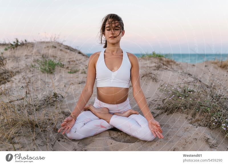 Young woman meditating while sitting on beach color image colour image outdoors location shots outdoor shot outdoor shots sunset sunsets sundown atmosphere