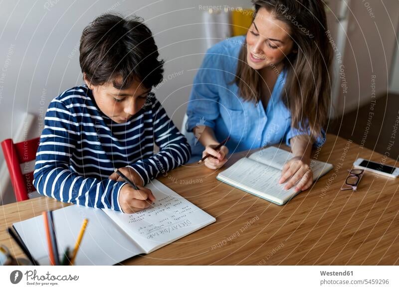 Young woman assisting boy in writing homework on table at home color image colour image Spain casual clothing casual wear leisure wear casual clothes