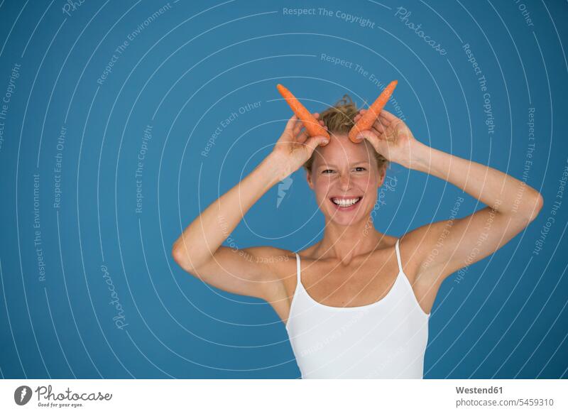 Smiling blond woman holding carrots, blue background human human being human beings humans person persons caucasian appearance caucasian ethnicity european 1