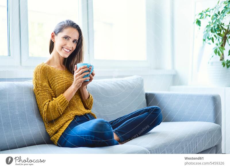 Beautiful young woman sitting on sofa drinking coffee and looking at camera human human being human beings humans person persons celibate celibates singles