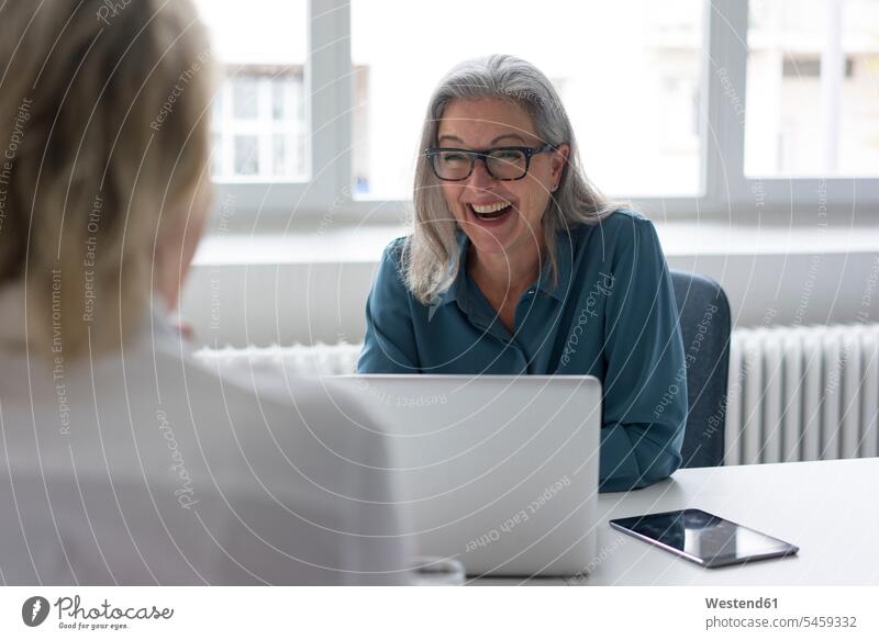 Laughing mature businesswoman talking to young businesswoman at desk in office generation difference in age Occupation Work job jobs profession