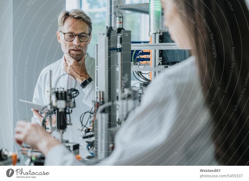 Thoughtful male scientist looking at machinery while working with female colleague in laboratory color image colour image indoors indoor shot indoor shots
