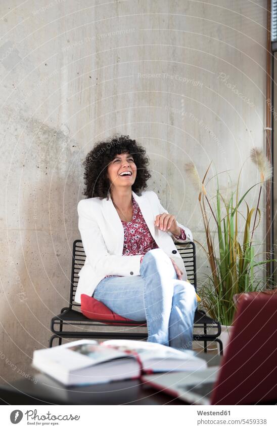 Happy businesswoman sitting on a chair at concrete wall concrete walls businesswomen business woman business women happiness happy chairs Seated business people