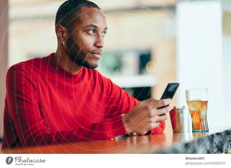 Pensive young man wearing red pullover at counter of a bar with soft drink and mobile phone pensive thoughtful Reflective contemplative bars refreshing drink
