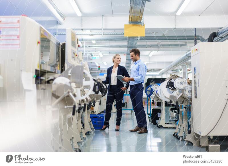 Male technician holding digital tablet while discussing with businesswoman standing by machinery at factory color image colour image indoors indoor shot