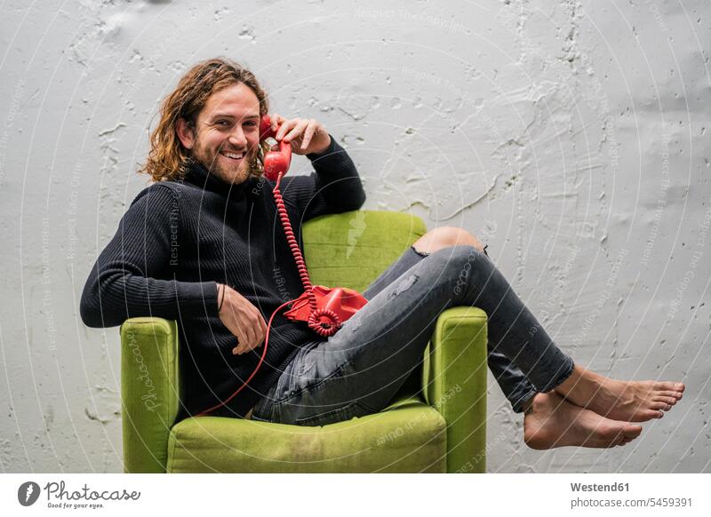 Smiling man talking over telephone while relaxing on armchair against wall color image colour image Spain leisure activity leisure activities free time