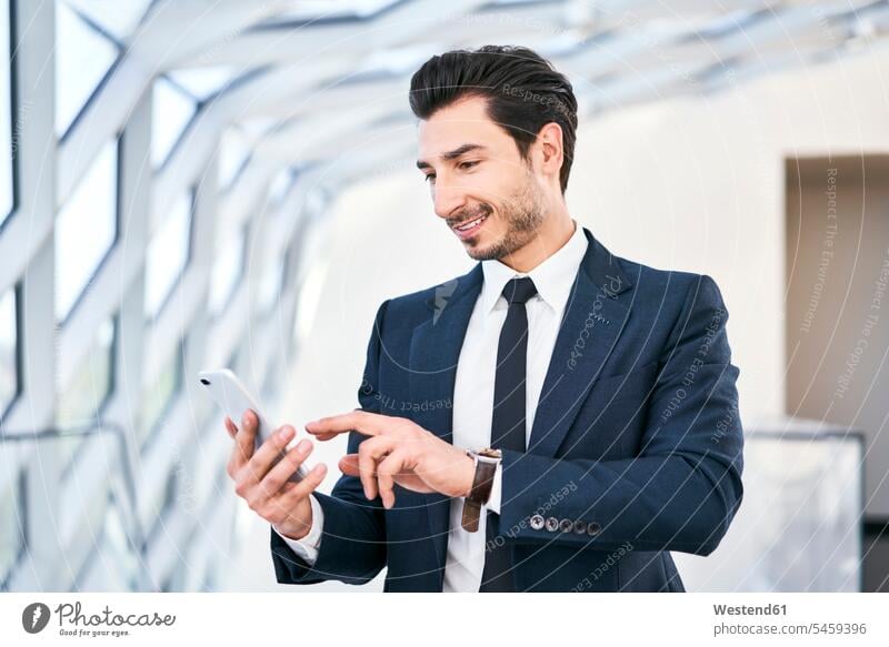 Smiling businessman looking at cell phone mobile phone mobiles mobile phones Cellphone cell phones eyeing Businessman Business man Businessmen Business men