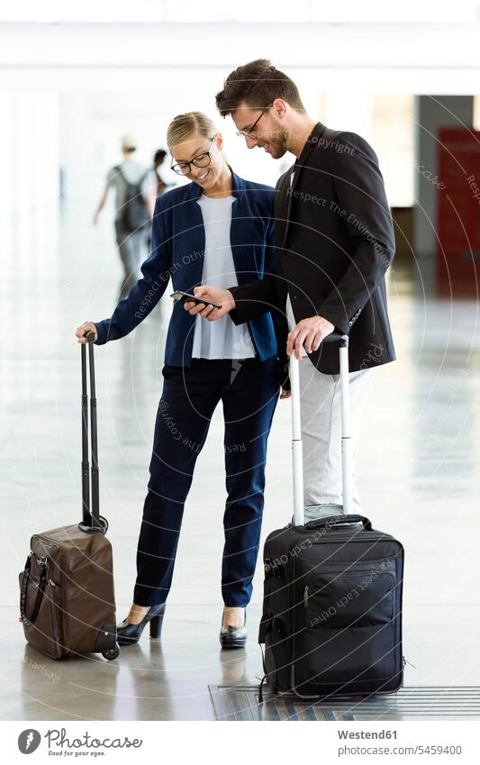 Two smiling young business partners using a smartphone at the airport business life business world business person businesspeople associate associates