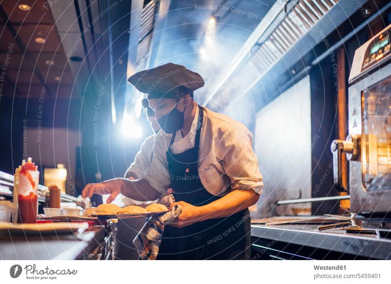 Chef wearing protective face mask preparing a dish in restaurant kitchen human human being human beings humans person persons 2 2 people 2 persons two