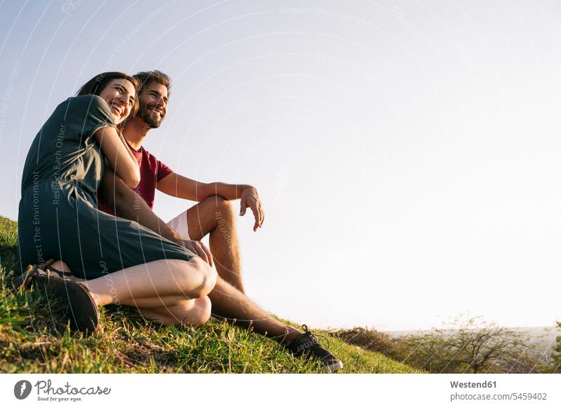 Woman embracing man while sitting on grass against clear sky color image colour image outdoors location shots outdoor shot outdoor shots sunset sunsets sundown