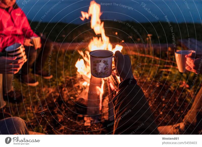Hand of person holding tea cup, group of people sitting at a camp fire warming up warm up hand human hand hands human hands Camp Fire Campfire Bonfire friends
