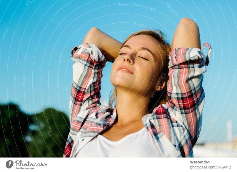 Woman with eyes closed hands behind head standing against clear sky color image colour image outdoors location shots outdoor shot outdoor shots day