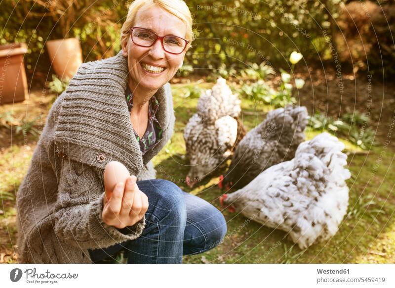 Portrait of happy woman in garden with her Orpington hens showing egg Germany nature natural world high spirits good mood Showing animal themes brown eggs
