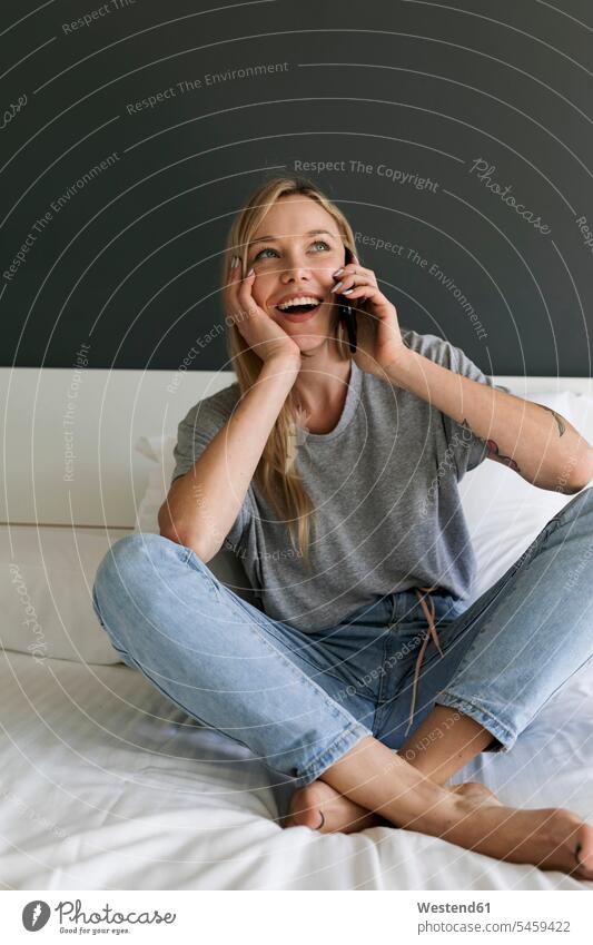 Happy young woman sitting on bed talking on cell phone mobile phone mobiles mobile phones Cellphone cell phones on the phone call telephoning On The Telephone
