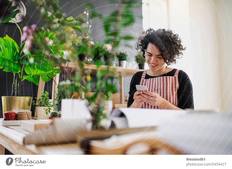 Smiling young woman using cell phone in a small shop with plants Occupation Work job jobs profession professional occupation human human being human beings