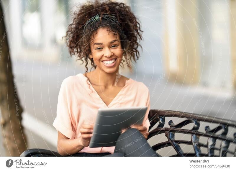 Portrait of happy young woman sitting on a bench using tablet happiness females women portrait portraits digitizer Tablet Computer Tablet PC Tablet Computers